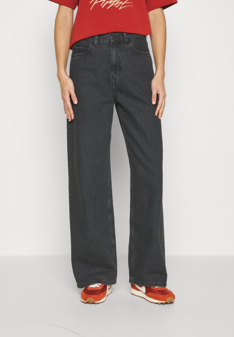 High-waisted wide-leg jeans in dark gray denim with a zip fly, five-pocket design, and slight faded texture, paired with red athletic shoes.