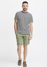 Stripete svart og hvit t-skjorte med kort erm og brystlomme, parret med rullede olivengrønne shorts og brune semskede sko.