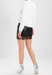 Un pull blanc duveteux, une jupe en cuir noir avec une bordure en dentelle, et des bottines argentées. Mettez l'accent sur la texture et le contraste de couleurs dans la tenue.