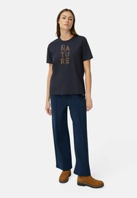 Marineblå T-shirt med korte ærmer og guld leopardprint "NATURE" tekst, parret med marineblå brede bukser og brune ankelstøvler.