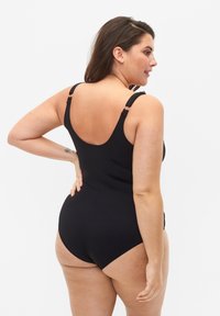 Maillot de bain noir une pièce avec bretelles ajustables, dos plongeant et tissu lisse. Présente des accents latéraux et une silhouette ajustée.