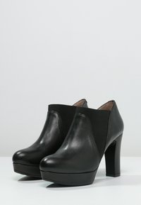 Bottines en cuir noir avec un bout arrondi, des panneaux latéraux élastiques et un talon épais. Texture lisse avec une semelle plateforme pour plus de hauteur.