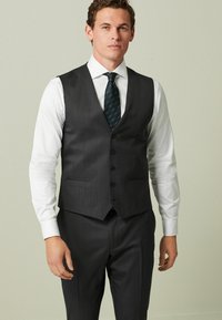 Graue Weste mit einem dezenten gestreiften Muster, fünf Knöpfen und vorderen Taschen, kombiniert mit einem weißen Hemd und einer dunkelgrünen gestreiften Krawatte.