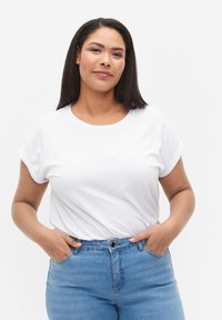 Camiseta blanca de manga corta con cuello redondo, combinada con jeans azul de cintura alta. Diseño sencillo con acentos de mangas enrolladas.