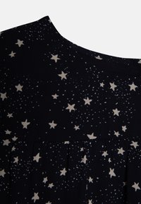 Tissu noir avec un motif d'étoiles beige clair. Col arrondi et détails plissés à l'ourlet. Texture lisse.