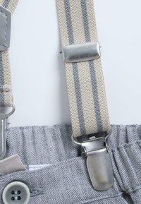 Ceinture élastique grise avec des bretelles rayées grises et crème. Clips en métal fixés à un tissu au fini texturé.