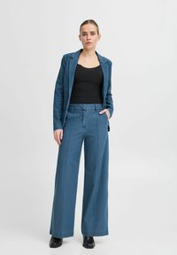 Blauwe denim blazer met een enkele knoop en wijde blauwe denim broek. Gestructureerde stof en zichtbare stikseldetails. Zwart mouwloos topje eronder.