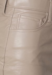 Beige Lederhosen mit einer glatten Textur, Nähdetails und einer klassischen Vorderertasche.