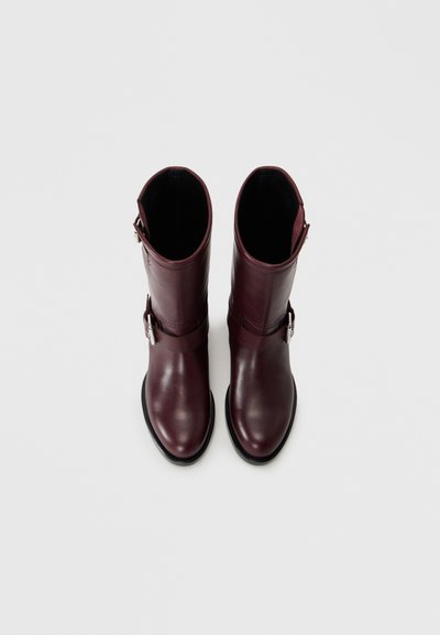 Burgundy leather knee-high boots with a smooth texture, featuring a side buckle detail and a rounded toe, resting on a black sole.