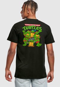 Black cotton t-shirt featuring a colorful graphic of four Teenage Mutant Ninja Turtles on the back, with bold text above the design.
