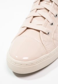 Beige lackläder sneakers med rund tå, platta texturerade snören, silverfärgade öglor och gummisulor med ett strukturerat mönster.