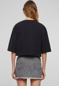 Černé zkrácené tričko s krátkými rukávy, spárované s vysokým šedým džínsovým sukní, která má roztrhaný lem a dvě zadní kapsy.