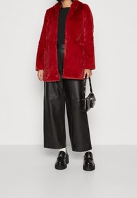 Rød faux fur frakke med hætte, der har en afslappet pasform og sidelommer. Kombineret med sorte læder bukser med vide ben og platform loafers.