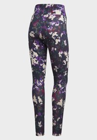 Högmidjade leggings med ett färgstarkt abstrakt kamouflage mönster i lila, svart, vitt, grönt och rött mot en ljus bakgrund.