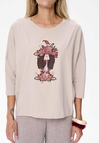 Vrouw in een beige top met een gestileerde gezichtsgrafiek versierd met bloemen, bladeren en een klein vogeltje op het hoofd.