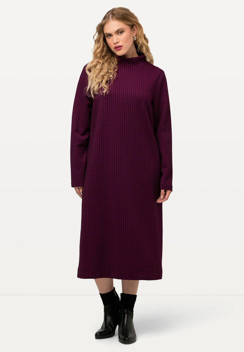 Langes lila Kleid mit langen Ärmeln und hohem Kragen, aus strukturiertem Stoff mit geometrischem Muster, kombiniert mit schwarzen Stiefeletten.