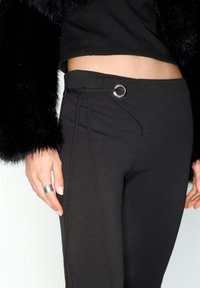 Schwarze, eng anliegende Hosen mit glatter Textur, ausgestattet mit einer Seitentasche, verstellbarem Kordelzug und einem silbernen Metallakzent.