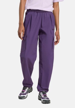 Purple cargo pants with an elastic waistband, pleats, and side pockets. Made from lightweight material, paired with black and gray hiking shoes.
