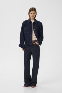 Veste en denim noir avec poches avant, associée à un pantalon en denim noir à jambes larges. Les deux ont une texture lisse et une coupe décontractée.