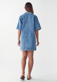 Denim jurk met een ontspannen pasvorm, korte mouwen en een kraag zoals een overhemd. Lichtblauwe kleur, tot halverwege de dij, met een achternaad en zijzakken.