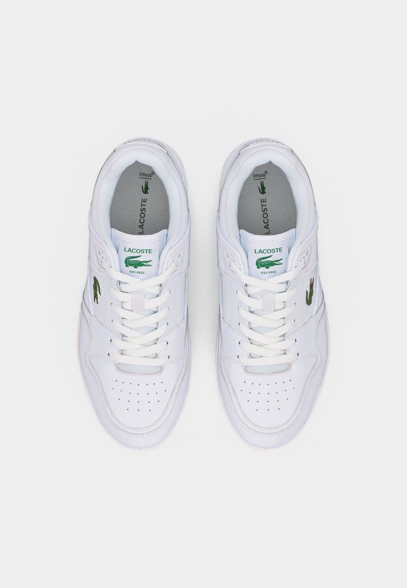 Een paar witte Lacoste sneakers met geperforeerde neuzen, groene krokodillenlogo's aan de zijkanten en op de tong, van bovenaf weergegeven op een witte achtergrond.