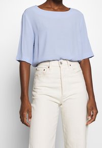 Blusa azzurro chiaro a maniche corte con scollatura ampia, abbinata a jeans a vita alta color crema. Tessuto morbido con vestibilità comoda.