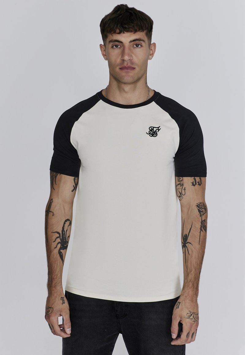 Camiseta raglán blanca y negra de manga corta, con un logo negro en el pecho y una textura suave de algodón.