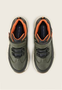 Baskets synthétiques vertes avec des accents orange, présentant une surface texturée, un col rembourré, une sangle à boucle velcro et des lacets noirs.