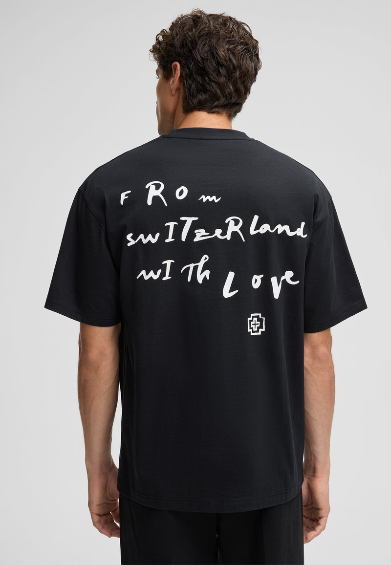 Schwarzes Baumwoll-T-Shirt mit weißem handgeschriebenem Text "FROM SWITZErLand WITH Love" auf dem Rücken und einem kleinen Logo in Weiß auf der unteren linken Seite.