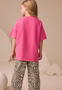 Tričko s krátkym rukávom v jasne ružovej farbe vyrobené z bavlny, v kombinácii s voľnými nohavicami s leopardím vzorom, ktoré majú čierne škvrny na béžovom pozadí.