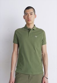 Olajzöld pamut póló, klasszikus gallérral, rövid ujjú, bal oldalon egy kis fehér logóval.