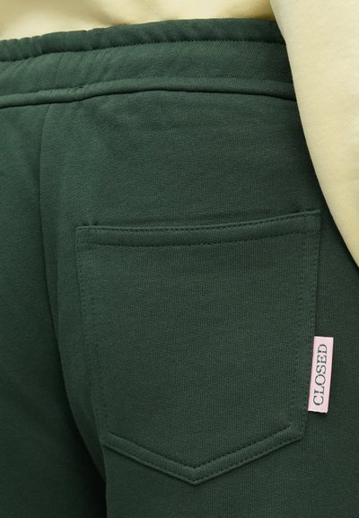Πράσινα βαμβακερά τζόγκερ με πίσω τσέπη σε ορθογώνιο σχήμα, υφή υφάσματος και μικρή ροζ ετικέτα με την ένδειξη "CLOSED".