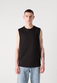 Tricou negru fără mâneci, cu decolteu rotund, din bumbac, asociat cu blugi de denim albastru deschis; textură netedă și croială casual.