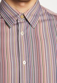 Gros plan sur une chemise à rayures verticales multicolores avec un col classique et des boutons beige, blanc et jaune.