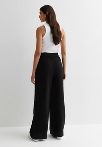 Zwarte wijde broek van textuurstof, met een elastische tailleband. Gecombineerd met een witte mouwloze top en witte sneakers.