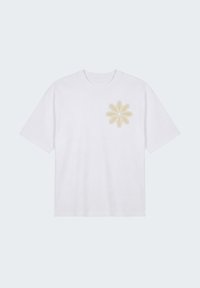 T-shirt blanc à manches courtes avec col rond et motif de fleur beige brodé sur le côté gauche de la poitrine.