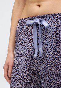 Lyse lilla pyjamasbukser med mørkt leopardprint, med elastisk talje, snøre med branding og blød stofstruktur.