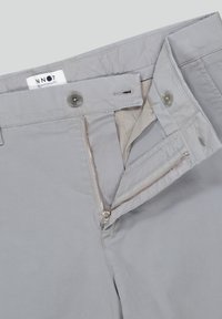 Pantaloni grigi in cotone con zip e chiusura a bottone, cuciture tono su tono e etichetta interna. Texture liscia e design casual.