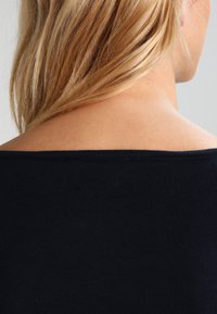 Marinblå ribbad stickad topp med en bred av-axeln halsringning. Sl ät textur med en figurnära silhuett som framhäver axlar och halsringning.