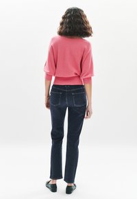 Maglione rosa a maglia con maniche a tre quarti, abbinato a jeans di denim blu scuro. L'outfit è completato da scarpe nere basse.