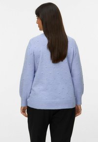 Pullover blu chiaro con una superficie testurizzata e punti in rilievo, maniche lunghe e orlo a costine. Indossato con pantaloni neri.