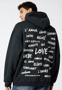 Felpa nera con un grande grafico testuale bianco sul retro, che mostra varie traduzioni di "amore" in diverse lingue.