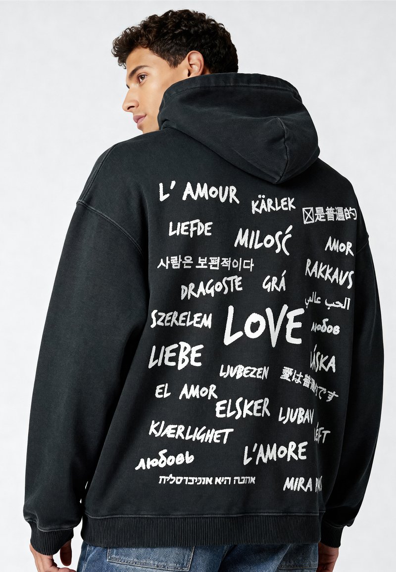 Felpa nera con un grande grafico testuale bianco sul retro, che mostra varie traduzioni di "amore" in diverse lingue.