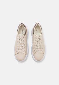 Sneakers in pelle beige con punta arrotondata, lacci piatti e suola in gomma bianca. Il tallone presenta un sottile accento marrone.