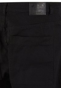 Svarta jeans med en stor bakficka och en strukturert läderetikett med varumärkning. Tyget är hållbart med en slät yta.
