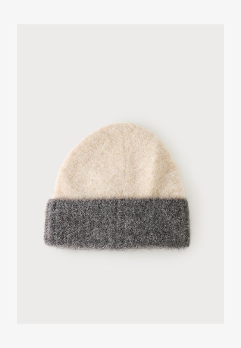 Bonnet en laine doux avec un dessus beige et une large bande de revers pliée gris foncé sur un fond uni.