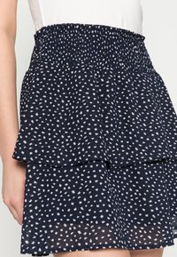 Navy blue, layered skirt with a smocked waist. Features a scattered white geometric pattern. Made from lightweight, textured fabric.