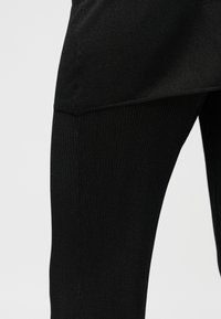 Μαύρα ριμπ κολάν με λεία, ελαστική υφή και σχεδιασμό με ψηλή μέση. Κοντινή όψη που αναδεικνύει τις λεπτομέρειες του υφάσματος.