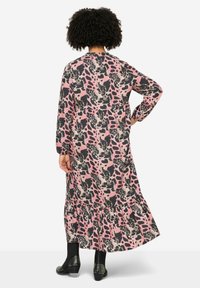 Robe longue à motifs présentant des couleurs rose, noir et crème avec un ourlet à volants. Fabriquée en tissu léger, avec des manches longues et une coupe décontractée.