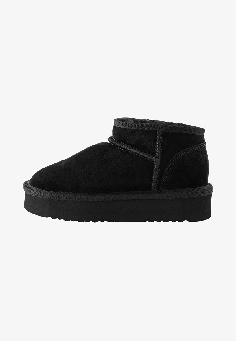 Black suede ankle boot with a rounded toe, stitched detail, and a flat rubber sole. Designed with a low upper and minimal accents.